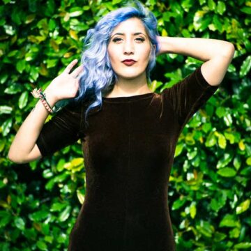 Model Kimiya Khosrovani posing confidently with vibrant blue hair against a lush green backdrop in Tustin, CA, captured by Coldea Productions.