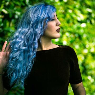 Fashion portrait of model Kimiya Khosrovani with blue hair against a lush green background in Tustin, CA, photographed by Coldea Productions