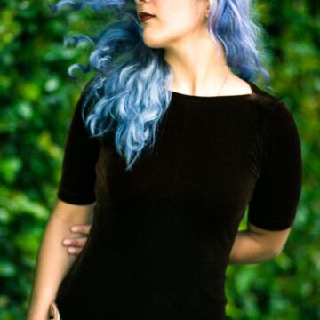 Kimiya Khosrovani posing outdoors with flowing blue hair and a dark dress, shot in Tustin, CA, showcasing fashion portrait photography.