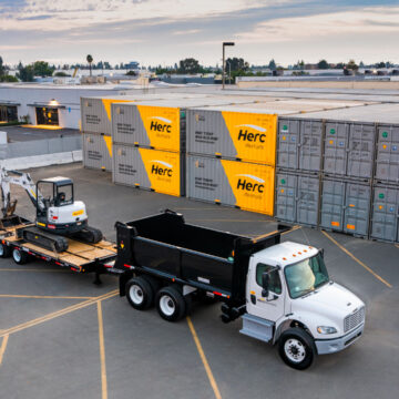 Aerial view of Herc Rentals truck and trailer loaded with construction equipment in an industrial lot, captured by Coldea Productions' drone and aerial photography services