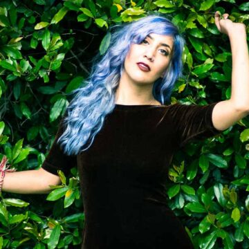 Portrait of model Kimiya Khosrovani with blue hair posing against a lush green foliage backdrop in Tustin, CA, showcasing Coldea Productions' expertise in fashion and portrait photography