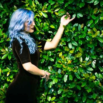 Portrait of model Kimiya Khosrovani with blue hair posing against lush greenery, captured in Tustin, CA by Coldea Productions.