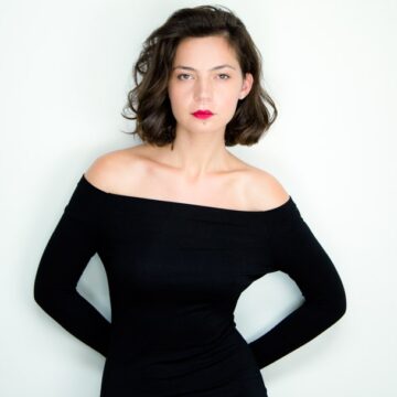 Maria-Dinulescu Professional headshot of a woman in a black off-shoulder top against a white background, captured by Coldea Productions.