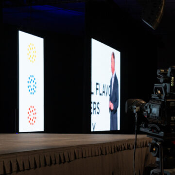 Convention-Photography Camera operator filming two speakers on stage at the Scentsy conference, captured by Coldea Productions, showcasing professional event production.
