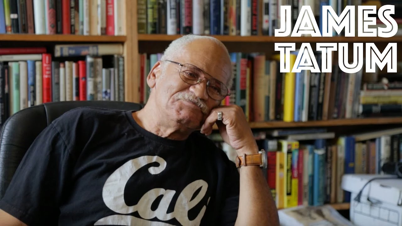 A cover image for a video story featuring James Tatum, the owner of Aldine Bookstore in Los Angeles, one of the last remaining bookstores in the area. James is seen seated in front of a shelf full of books, wearing a casual "Cali" t-shirt and glasses, exuding a thoughtful expression.