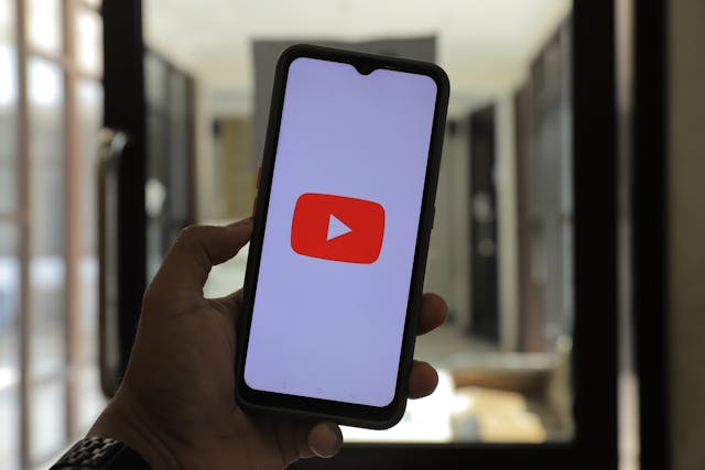 A man holding a phone and opening the YouTube app. 
