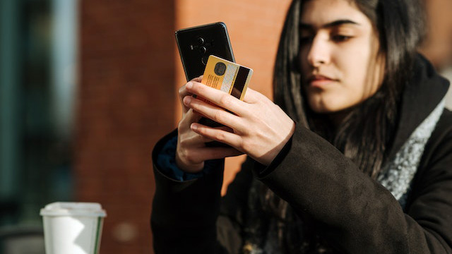 A young woman using a smartphone while holding a credit card.