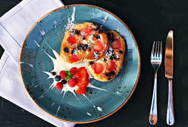 Artistic food photography of a plate with berry-studded pancakes, garnished with powdered sugar, fresh berries, and a drizzle of cream.