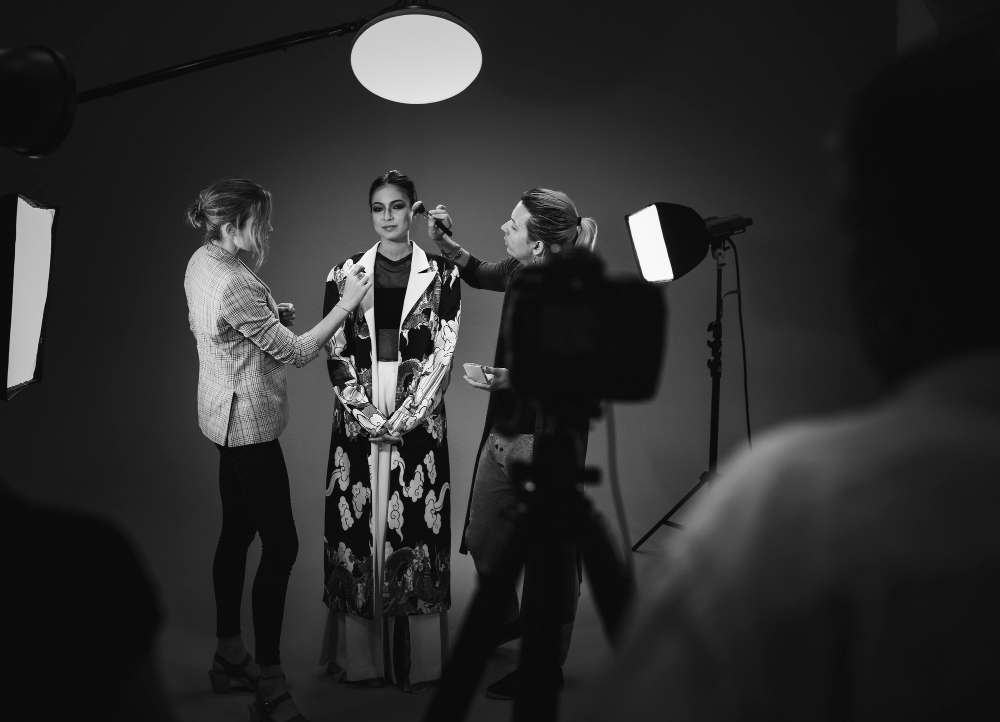 Model receiving makeup and styling touch-ups during a fashion photo shoot on the set of Coldea Productions.