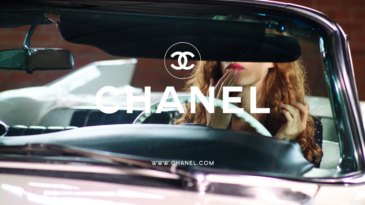 Woman applying lipstick in a vintage car for Chanel video presentation.