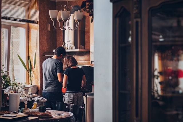 A couple cooking together in a warm, inviting kitchen filled with natural light and personal touches, emphasizing the lifestyle appeal of a home.