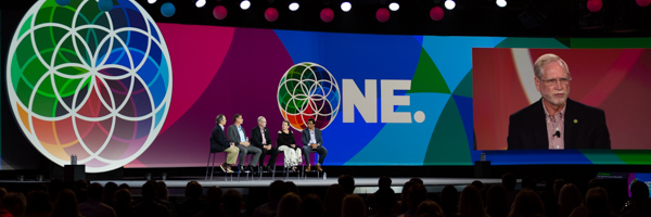 A panel discussion on stage with vibrant visuals and a large audience, showcasing professional convention event photography by Coldea Productions