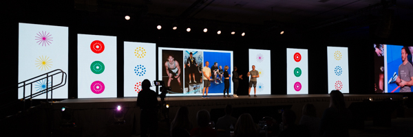 A live event setup with vibrant digital screens and a stage featuring presenters, highlighting the capabilities of professional live streaming and event photography.