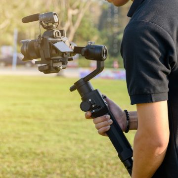 Person holding a camera mounted on a gimbal stabilizer outdoors, capturing smooth and steady video footage in a natural setting.