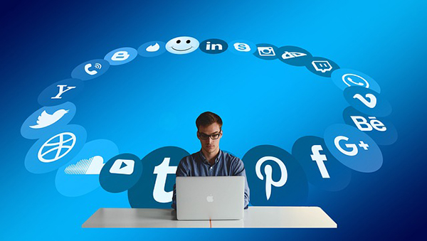 A man working on a laptop surrounded by social media icons, representing the importance of incorporating visual elements in online posts.