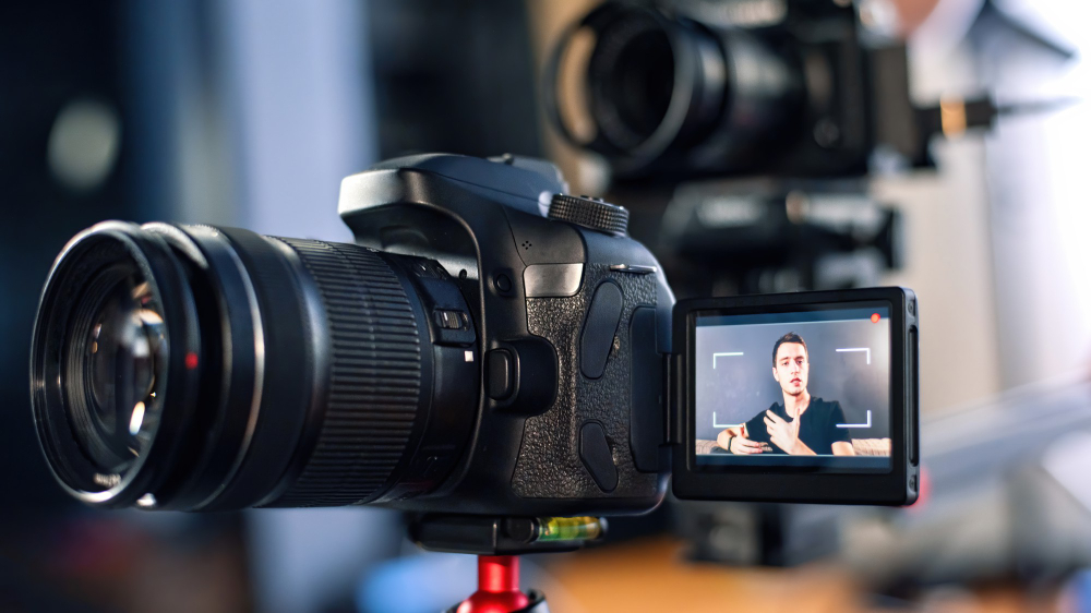 Man recording himself on a DSLR camera for a vlog, with multiple cameras set up in a studio environment.