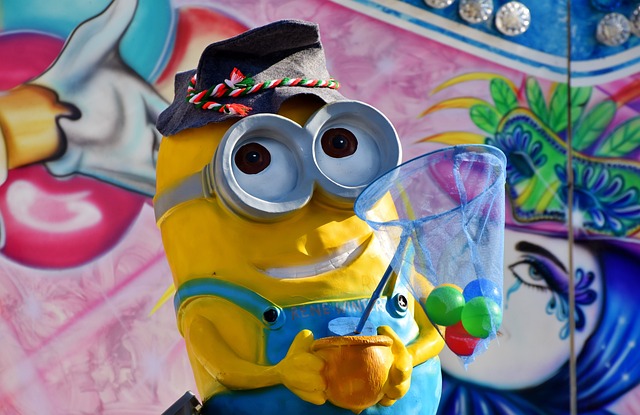 A Minion character wearing a hat, holding a net with colorful balls, standing in front of a vibrant, decorative background.