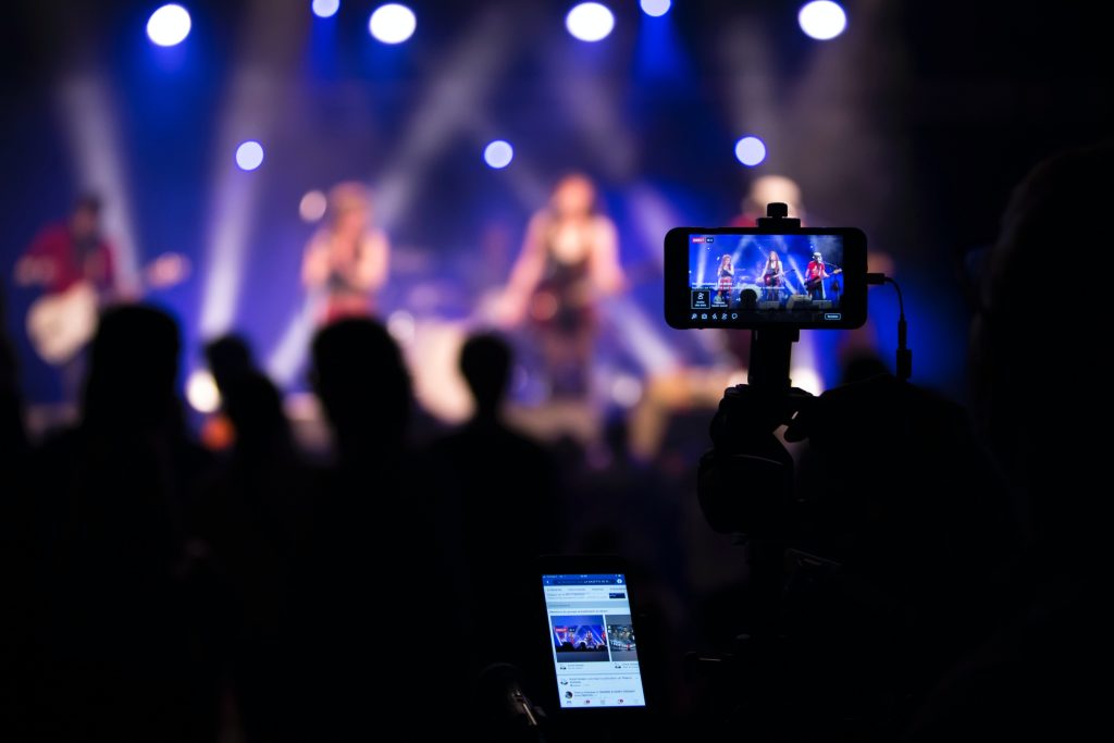 A live concert being filmed and streamed online using a smartphone mounted on a tripod.
