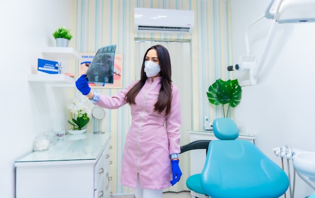 Orthodontist in pink uniform reviewing a dental X-ray inside a modern clinic, representing expertise and trust in NYC orthodontic case studies.