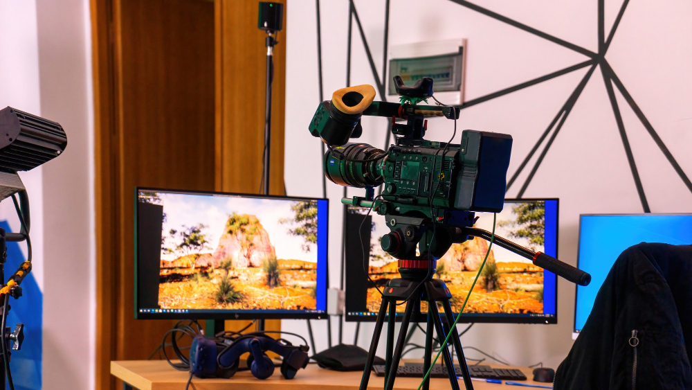 Professional video camera set up on a tripod in a studio, with dual monitors displaying a virtual production scene.