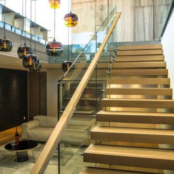 Modern interior staircase with floating wood steps, glass railings, and artistic pendant lighting, captured by Coldea Productions for real estate photography.