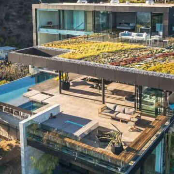 Aerial view of a modern hillside luxury home with a green rooftop, large patio, and pool, photographed by Coldea Productions