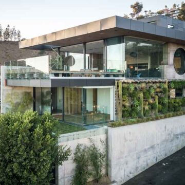 A modern luxury home with expansive glass walls and green architectural features, showcasing Coldea Productions' real estate photography services.