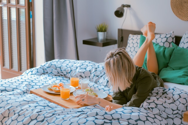 A woman relaxing on a bed with a breakfast tray featuring juice and food, showcasing a cozy and inviting lifestyle, perfect for highlighting home amenities in a real estate lifestyle video.