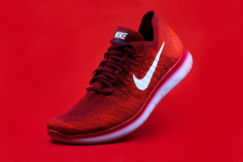 Close-up of a red Nike Flyknit running shoe on a vibrant red background.