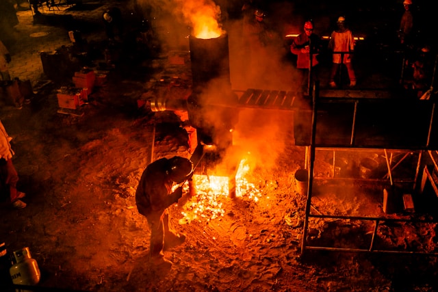 An artist pouring molten iron during an iron casting process, surrounded by fire and heat.