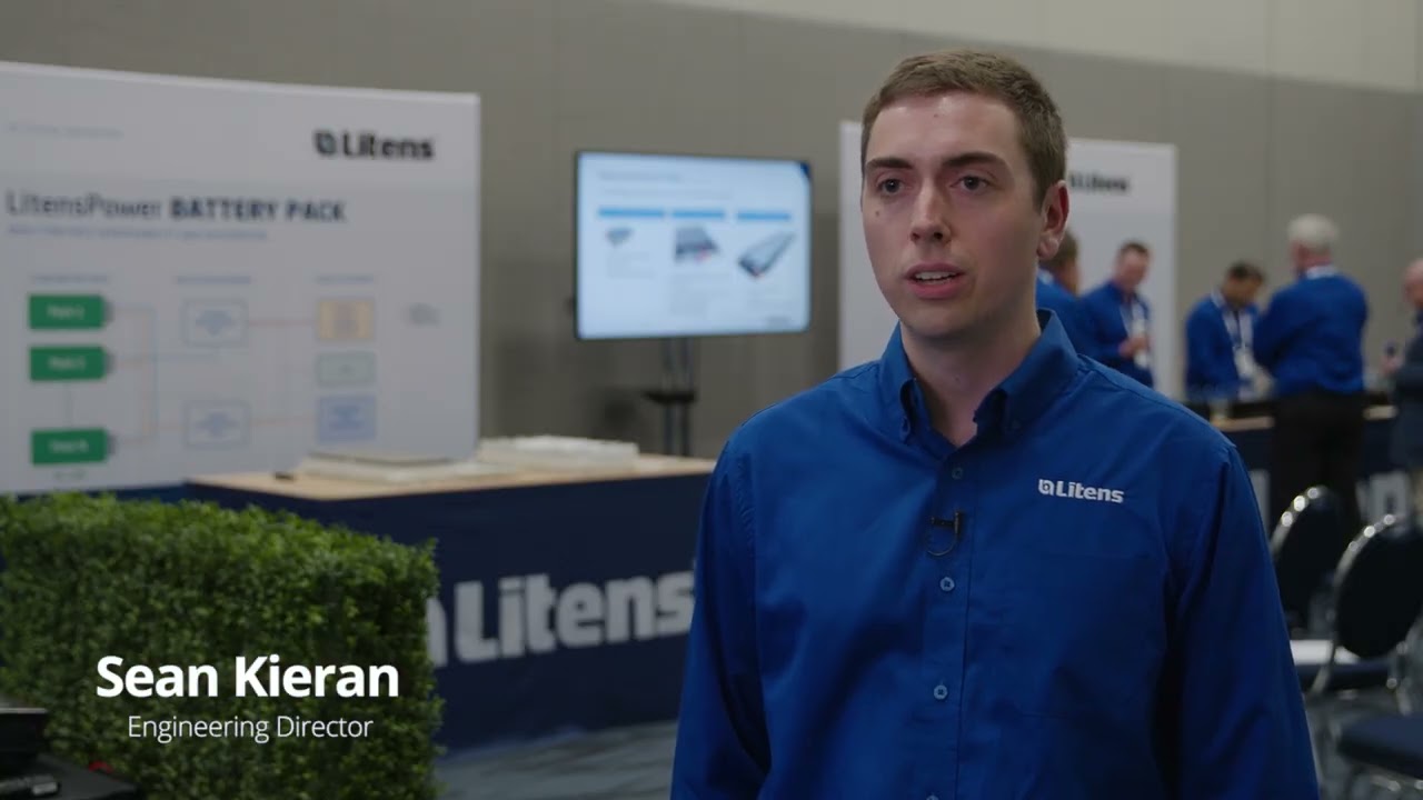 Sean Kieran, Engineering Director at Litens, gives an interview at a trade show booth with company branding and technical displays in the background.