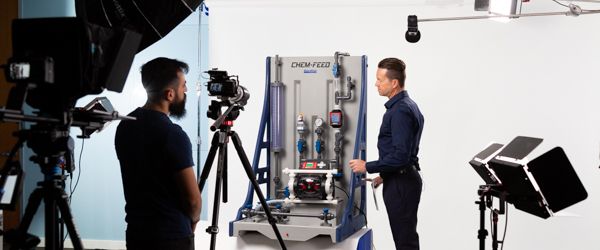 This behind-the-scenes image shows Alexis Mendez and Alex Stoica from Coldea Productions filming a Blue-White Peristaltic Metering Pump. Coldea Productions specializes in high-quality product videography, setting up professional lighting and equipment to capture detailed visuals for Blue-White Industries.