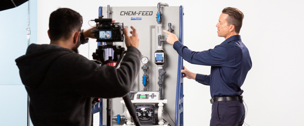 Rob Gledhill from Blue-White Industries demonstrates the functionality of Plastic Chemical Feed Skids while Alexis Mendez from Coldea Productions captures the video presentation.