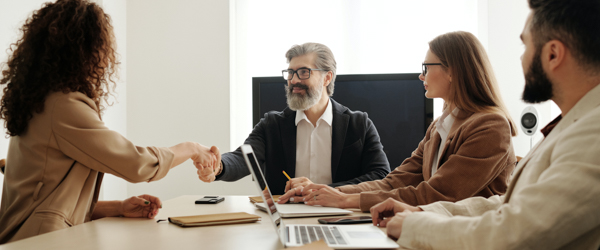 A professional business meeting where a manager shakes hands with a team member, representing collaboration and learning in a corporate environment.