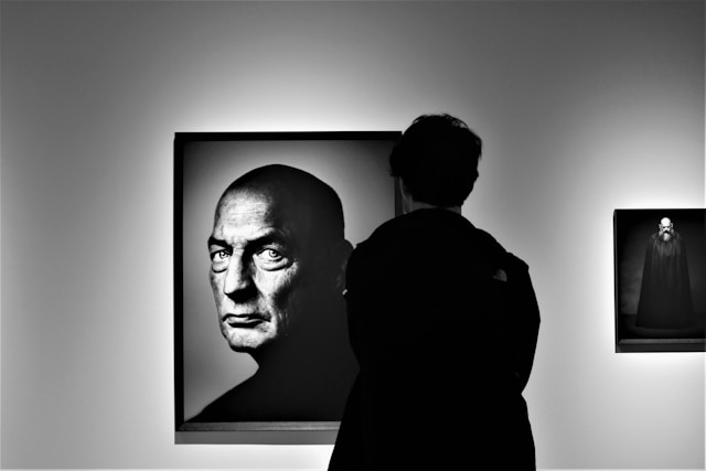 Person observing a black-and-white portrait in an art gallery, symbolizing how professional photography frames perception and builds emotional connection, by Coldea Productions.
