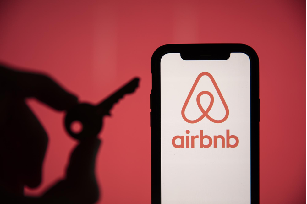 A smartphone displaying the Airbnb logo with a silhouette of a key in the background, representing Airbnb hosting and property management.